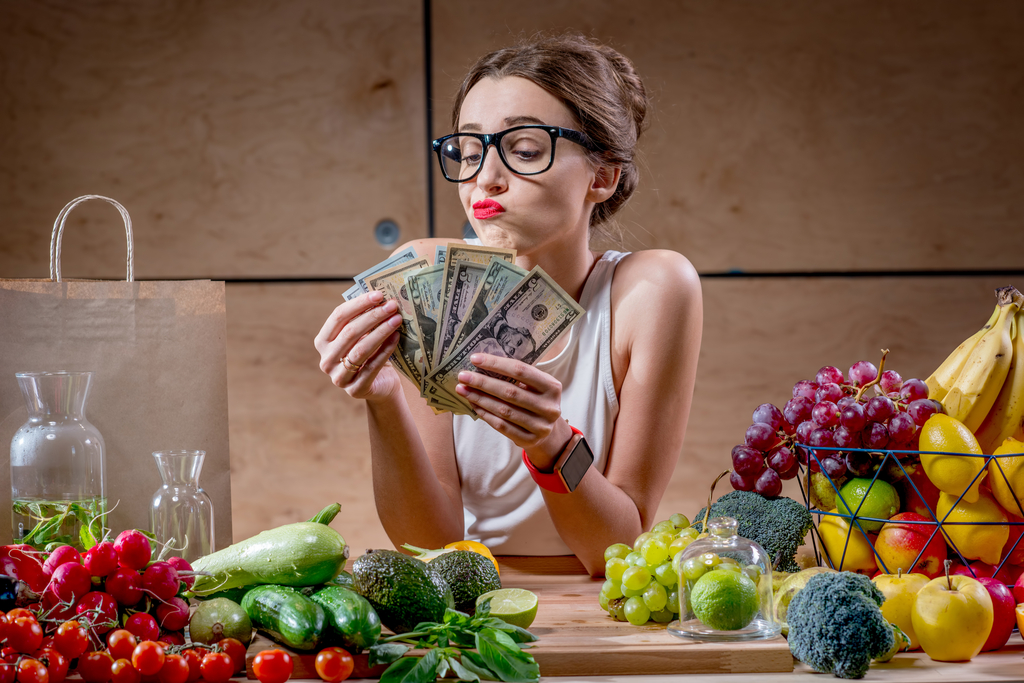 Female holding money while overlooking vegetables and fruits.