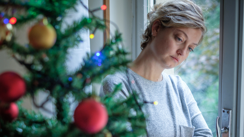 Woman leaning against a window looking towards a Christmas Tree.