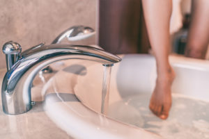 Picture of someone stepping into a bath as it fills with water.